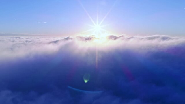 Aerial flight above glowing clouds at sunset with golden sunlight breaking through. Cinematic skyscape with soft fog, warm colors and dramatic atmosphere high above the horizon.