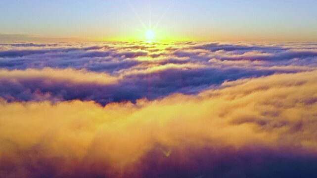 Aerial flight above glowing clouds at sunset with golden sunlight breaking through. Cinematic skyscape with soft fog, warm colors and dramatic atmosphere high above the horizon.