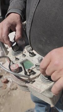 Vertical video. Professional operator managing a concrete pump at a construction site using a radio remote control, manipulating joysticks and buttons to precisely guide the industrial equipment