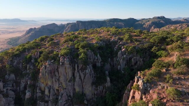 Stunning aerial drone footage soaring over dramatic rocky cliffs and rugged mountain ridges covered with green vegetation during golden hour.