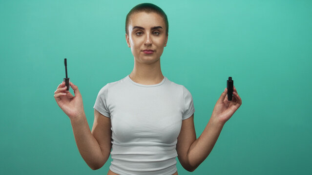 Young woman holding mascara wand in both hands, winking and presenting tube in studio; confidence beauty.