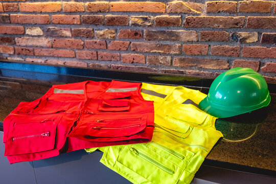 Construction safety equipment including green hard hat, red and yellow safety vests arranged on table with brick wall background at construction site