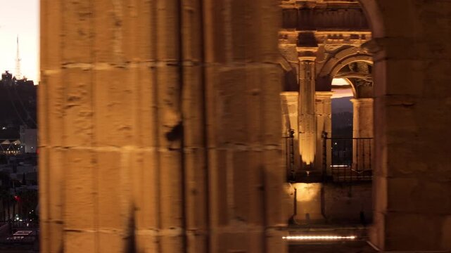 Aerial drone footage orbits around the illuminated bell tower of Cathedral Basilica of Immaculate Conception in Durango, Mexico during sunset with city lights below and mountains in background.