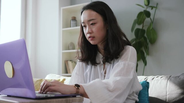 Shooting of calm sweet Chinese young woman wearing white blouse touching keyboard of laptop. Footage of working pretty girl. Flat. Inside.
