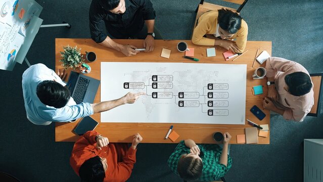 A diverse group of professionals collaborates around a large table, engaging in a productive meeting focused on data analysis and concept mapping. Raster