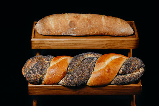 Braided poppy seed and plain loaves on wooden display stand in bakery setting