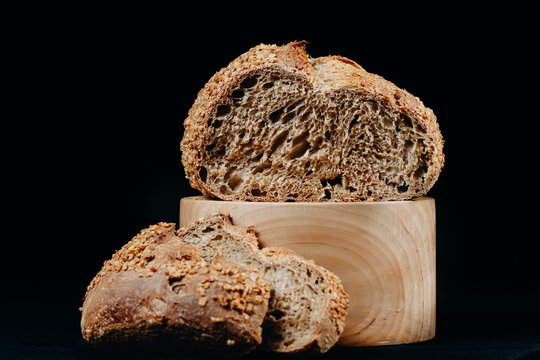 Rustic whole grain bread loaf and slices on wooden block against black background
