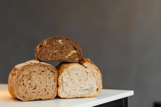 Three artisan bread loaves stacked on a marble counter with sliced sourdough and wholegrain textures