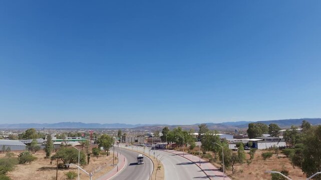 Aerial drone footage captures sprawling urban landscape of Durango, Mexico with industrial warehouses, main road, and distant Sierra Madre mountains under clear blue sky.