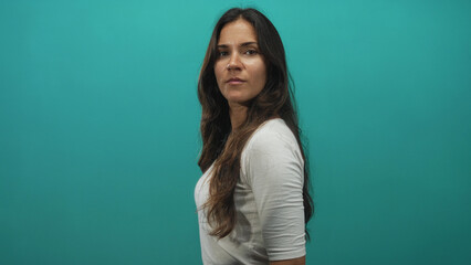 Fototapeta premium Woman standing in profile showing face and long hair in studio with teal wall; calm personal contemplation.
