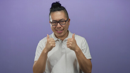 Obraz premium Young chinese man smiling and giving two thumbs up in purple studio wearing white polo shirt; positive approval.