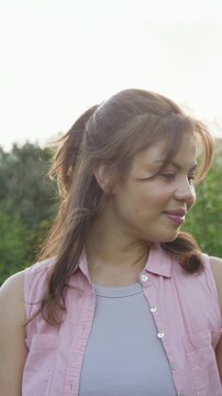 Vertical video: Camera zooming, woman reacting, turning and laughing in woods wearing pink shirt