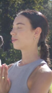 Vertical video: Starting session, woman in tank top holding prayer pose in park, meditating