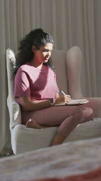 Vertical video: Taking notes with notebook woman in mauve top and watch sitting in bedroom studying