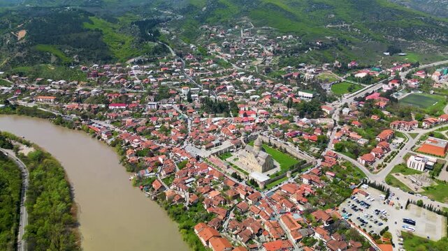 Aerial view of a historic town with red-roofed houses and a large cathedral surrounded by a river landscape.