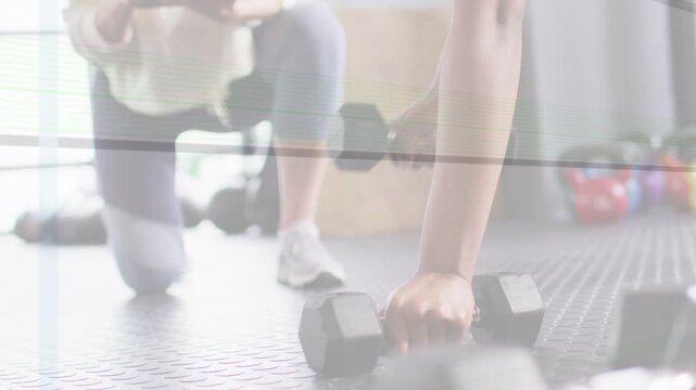 Fitness coach cueing client while holding plank, lifting hex weights and noting form for strength