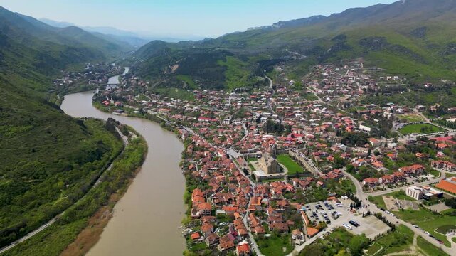 Aerial view of a historic town with red-roofed houses and a large cathedral surrounded by a river landscape.
