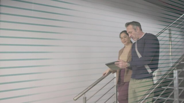 Colleagues descending stairs, pulling tablet, swapping and reviewing business, stripes crossing