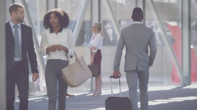 Man in gray suit rolling suitcase walking away, drawing camera to business colleagues conversing
