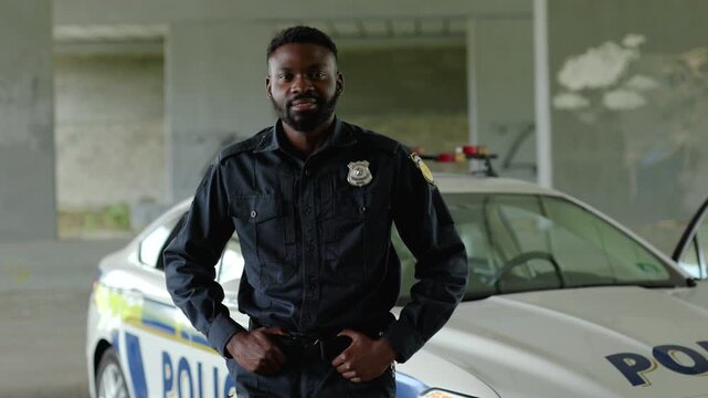 A police officer is standing next to his cruiser in a deserted location, ready to assist