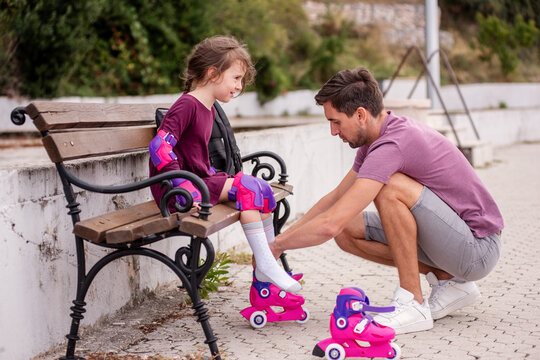 Father helping daughter with roller skates at park