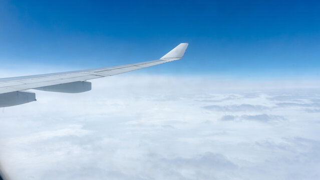 Airplane wing soaring above clouds in clear blue sky