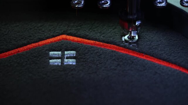 Machine embroidery on a black fleece blouse with red thread. House roof embroidery. Selective focus close-up.
