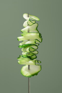 Fresh sliced cucumber ribbons on skewer on green backdrop