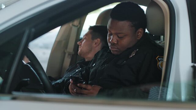 Handsome young men cops sitting use phone in patrol car accepting emergence call enforcement talk african american officer police uniform auto safety communication control policeman slow motion
