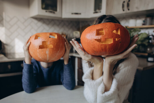 Brother and sister hide their faces behind carved pumpkin