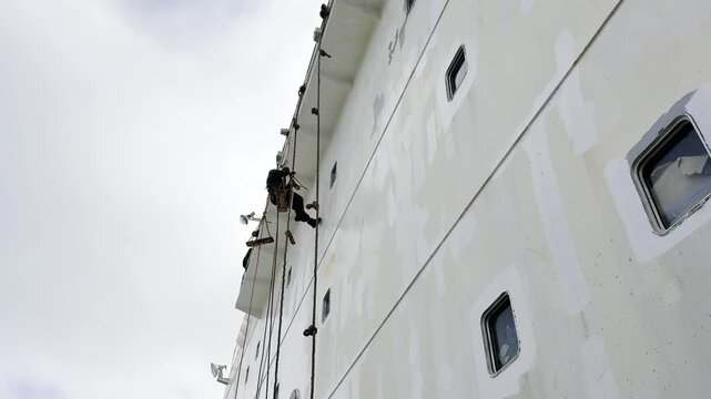 seafarers lean on the ropes during working aloft. make painting ship's superstructure. team work, cooperation. 