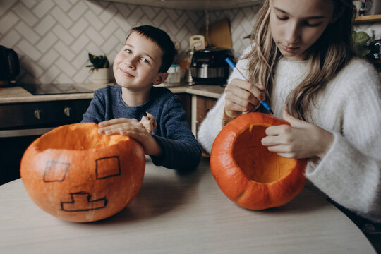 Siblings drawing jack-o-lantern faces on pumpkins at home