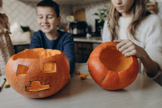 Siblings carving Halloween pumpkins at home kitchen table