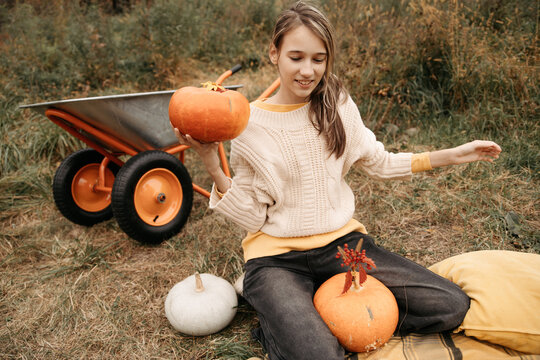 Girl with pumpkins sitting on grass in autumn countryside