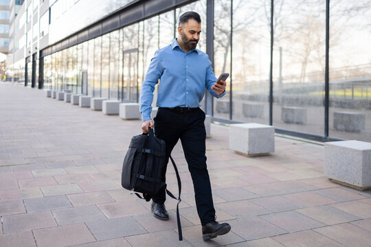 Arab businessman walking by office while checking smartphone