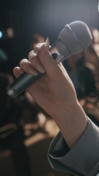 Vertical cropped closeup shot of unrecognizable businesswoman standing in front of audience and speaking into microphone giving lecture at conference