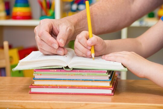 Adulte aidant un enfant &agrave; &eacute;crire dans un cahier avec un crayon, apprentissage et soutien scolaire &agrave; domicile