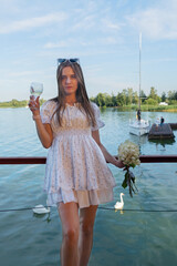Fototapeta premium A joyful woman is celebrating by the peaceful water, holding vibrant flowers and enjoying the beautiful view around her