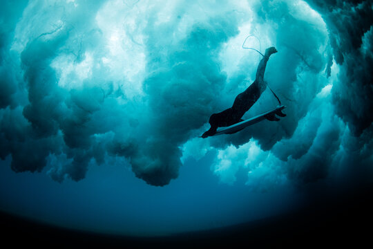 Surfer underwater beneath breaking wave in deep blue sea