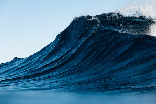 Dramatic blue ocean wave cresting under clear sky