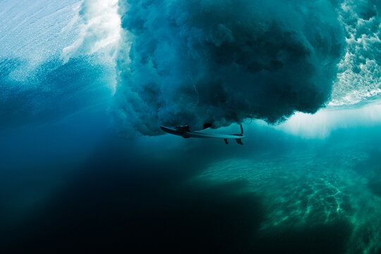 Underwater view of surfer beneath a powerful breaking wave