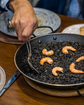 Spanish black rice paella with shrimp served at table