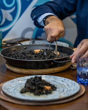 Serving Spanish black rice paella at a restaurant table