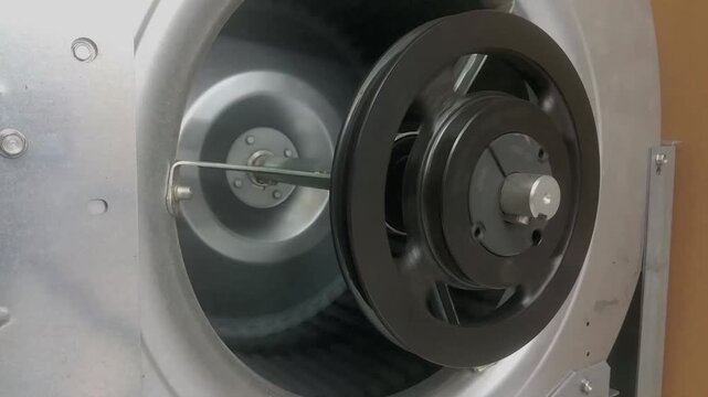 A close up shot of a scroll fan with its pulley in motion as it gradually slows down and comes to a stop