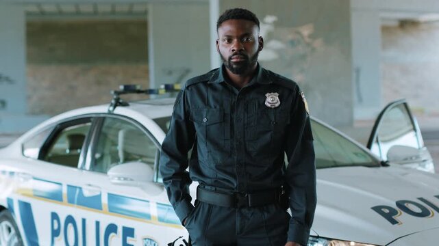 Serious young african american young man cops stand near patrol car look at camera enforcement happy officer police uniform auto safety security control policeman portrait close up slow motion