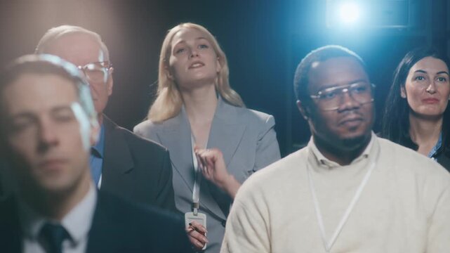 Arc zoom out shot of group of multiethnic business people listening attentively to speaker on stage with young blonde Caucasian woman asking questions during presentation