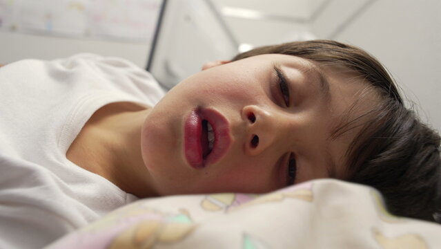 Sick child lying in hospital bed breathing weakly, close-up of exhausted young patient recovering after illness, emotion of fatigue and fragility in medical setting