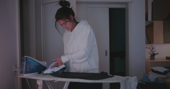 Woman concentrating while ironing and folding laundry, depicting dedication and care in quiet domestic evening routine at home