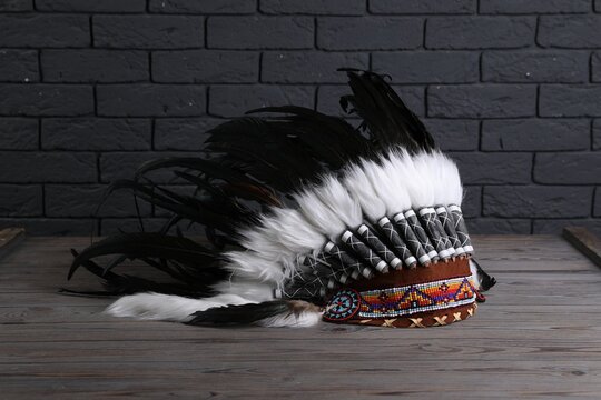Native American chief headdress (feathered war bonnet) on wooden surface against gray brick wall