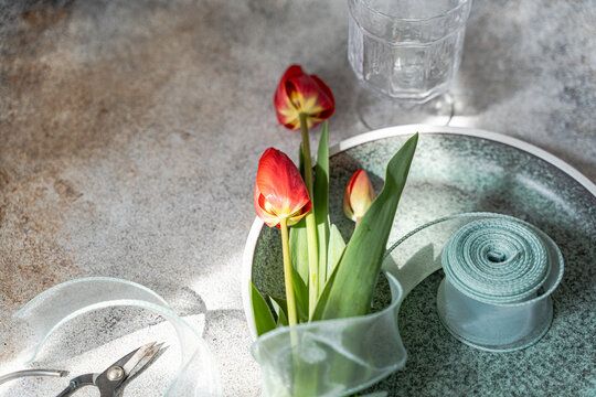 Red tulips on plate with ribbon, scissors and glassware